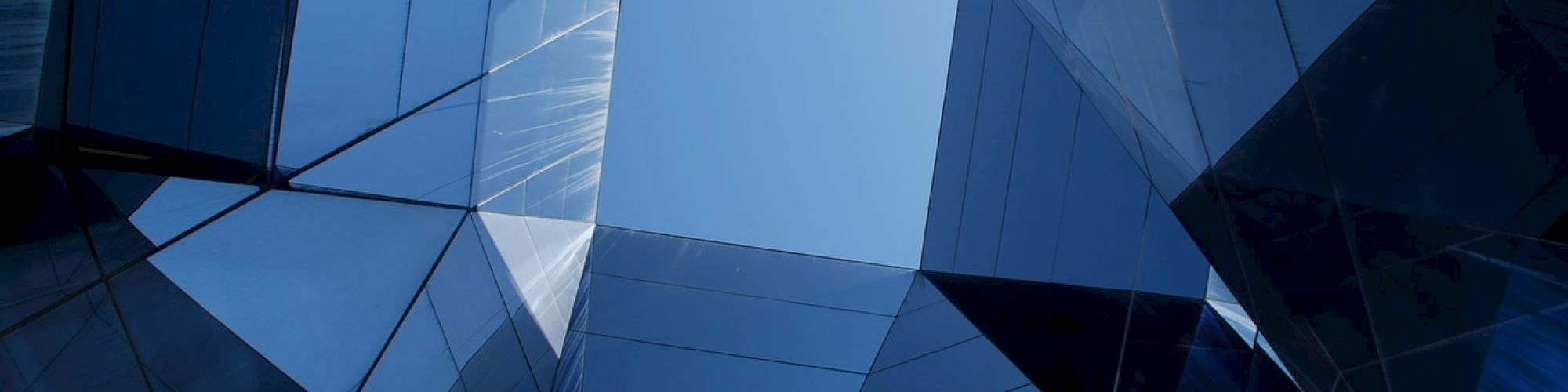 Geometric shapes in a building form a skyward view with reflections on glass surfaces, creating a modern architectural design.