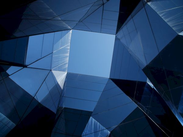 The image shows a geometric pattern of reflective glass panels, forming a skylight, with a clear blue sky visible through the center.