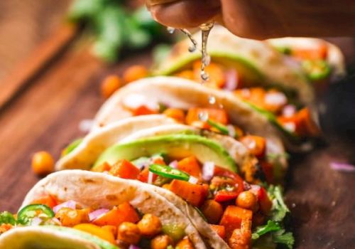 A hand squeezes lime over tacos filled with chickpeas, vegetables, and fresh cilantro, arranged on a wooden board with lime slices.