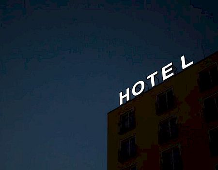 A building with illuminated "HOTEL" sign against a dark sky, with one letter "L" missing.