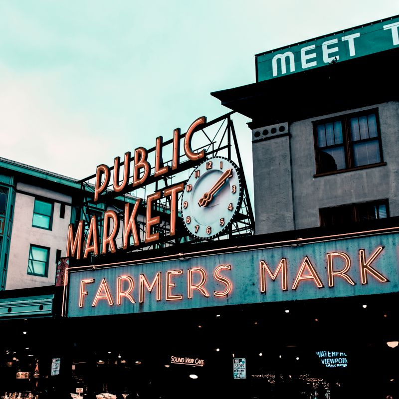 The image shows a large sign for a "Public Market" with "Farmers Market" below, featuring a clock. Buildings are visible in the background.