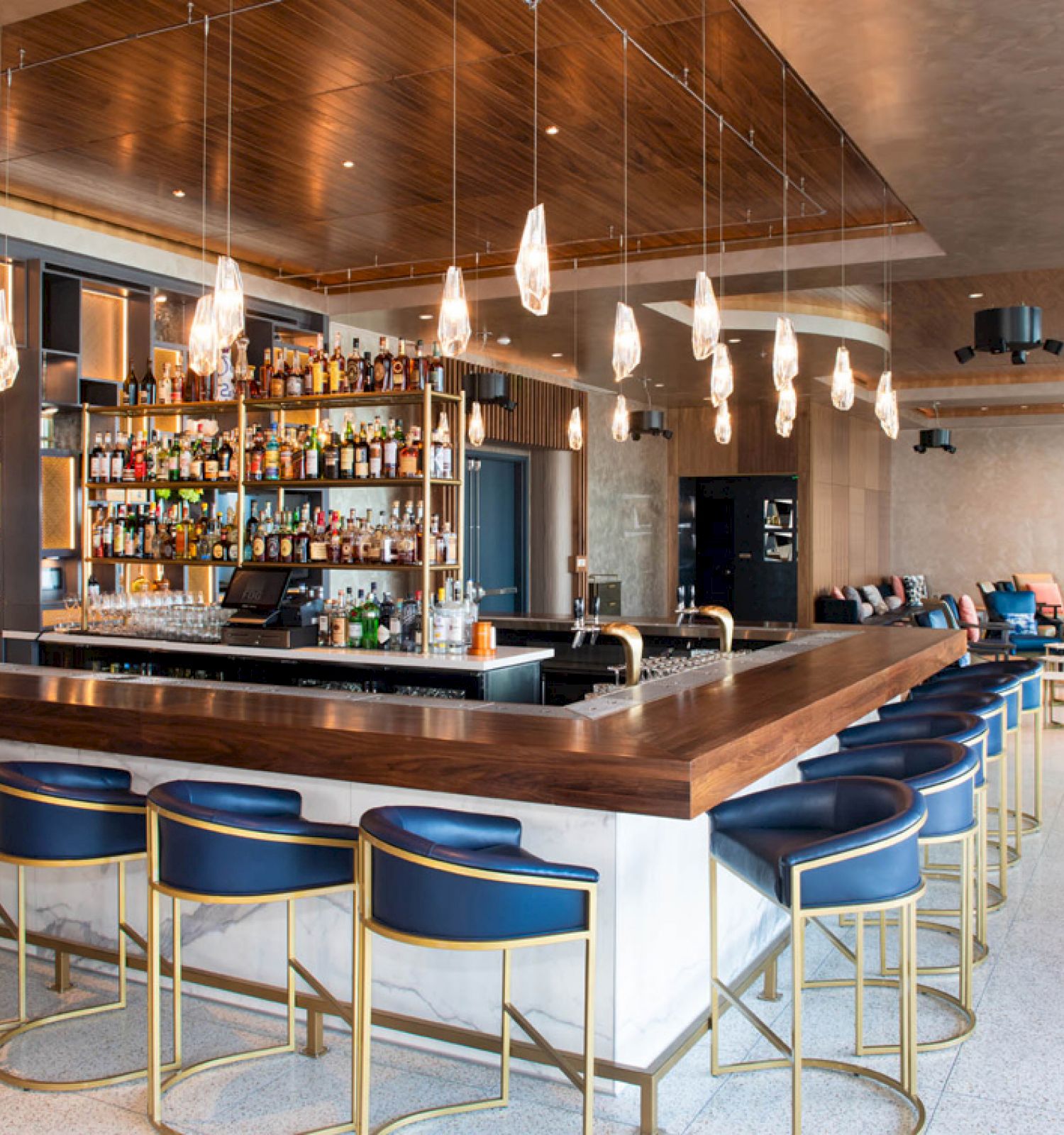 A modern bar with stylish blue stools, wooden accents, and hanging lights, featuring a well-stocked liquor display.