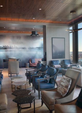 The image shows a modern lounge area with comfortable seating, large windows with a scenic view, and contemporary wall art.