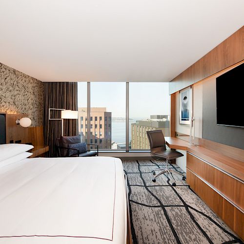 A modern hotel room with a large bed, wall art, flat-screen TV, and a view of city buildings outside the window completes the scene.
