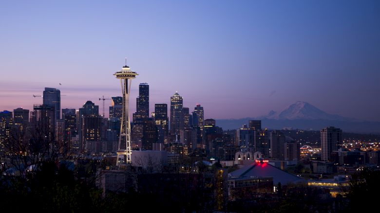 A city skyline at dusk featuring the Space Needle with Mount Rainier visible in the background under a clear sky.