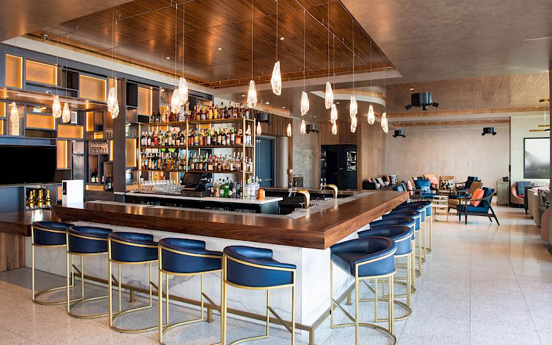 A stylish bar with blue stools, hanging lights, and a stocked liquor shelf. There's also a cozy seating area with armchairs.